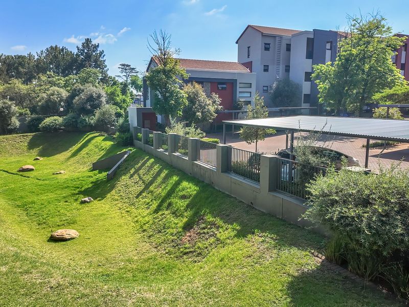 A well-maintained exterior view of the apartment complex featuring a landscaped garden, secure perimeter fencing, and covered carport parking.