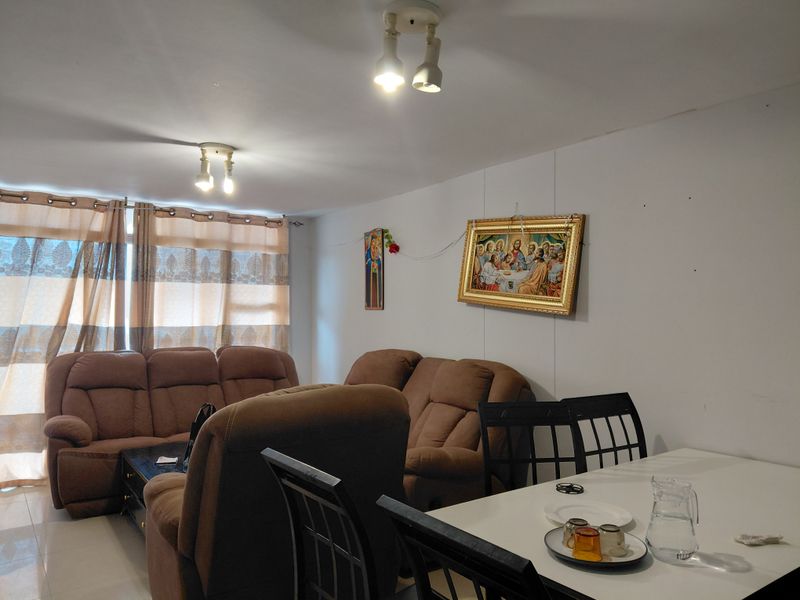 An open-plan living and dining area featuring tiled flooring and ceiling-mounted spotlights, offering a functional space for relaxation and meals.