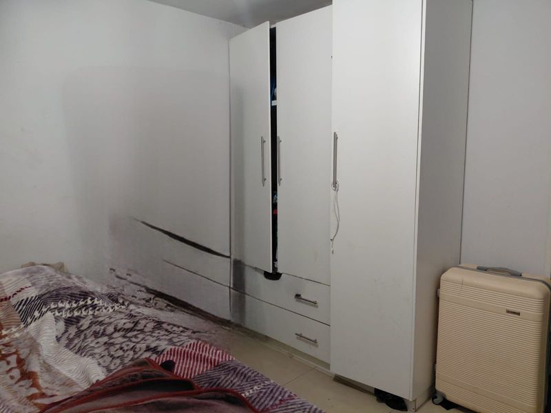 A bedroom featuring a white built-in wardrobe, showing significant wall staining and signs of potential moisture damage requiring attention.