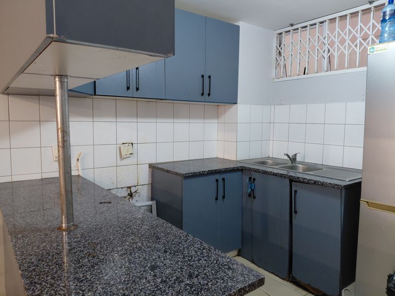 A functional kitchen featuring blue cabinetry, granite countertops, a double basin sink, and a tiled backsplash, ready for a modern update.