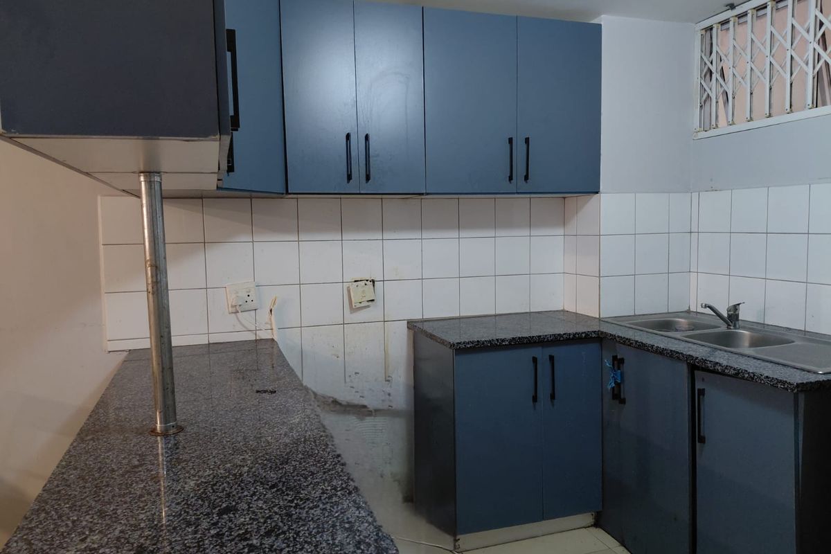 A functional kitchen featuring blue cabinetry, granite countertops, a double stainless steel sink, and a tiled backsplash, currently awaiting new appliances.