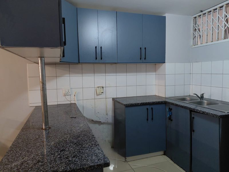 A functional kitchen featuring blue cabinetry, granite countertops, a double stainless steel sink, and a tiled backsplash, currently awaiting new appliances.