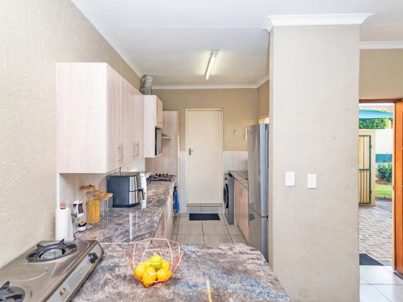 Functional kitchen featuring laminate cabinetry, stone-look countertops, built-in gas hob, and direct access to the exterior through a timber door.