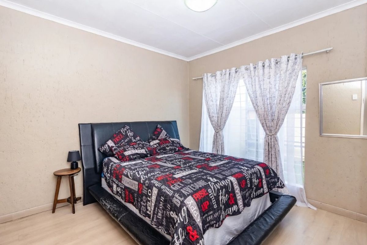 A well-lit bedroom featuring light-toned laminate flooring, neutral wall finishes, and a window dressed with curtains.