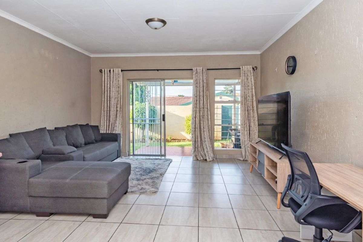 A spacious living room featuring neutral tiled flooring and a sliding glass door that provides direct access to the rear patio and garden area.