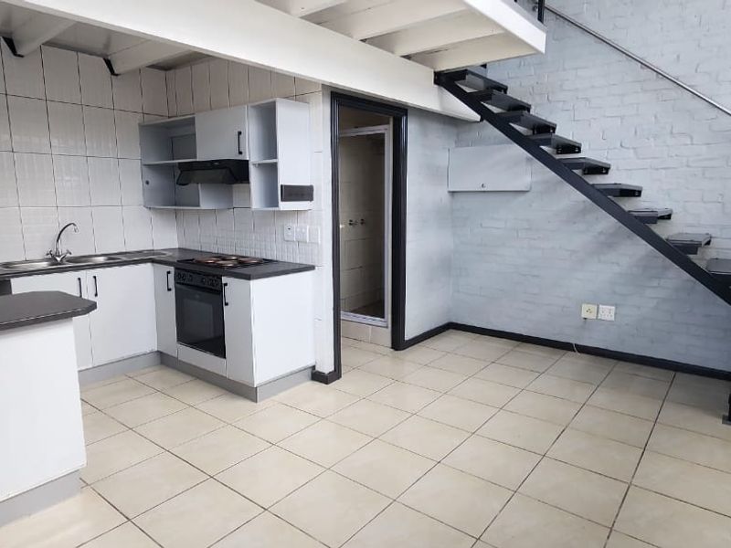 Open-plan living area featuring a functional kitchen with built-in appliances, tiled flooring, and a staircase leading to an upper level.