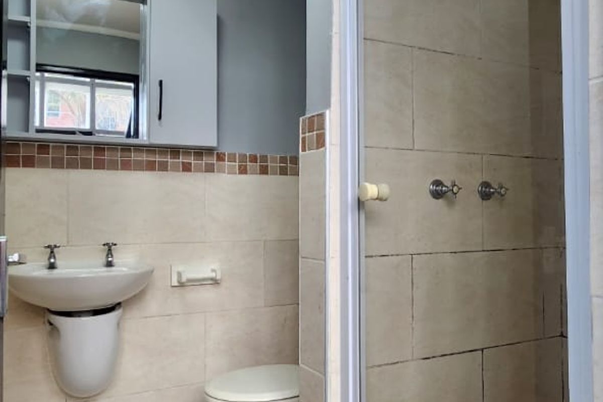 A functional bathroom featuring a wall-mounted basin, toilet, and a separate shower enclosure with tiled finishes throughout.