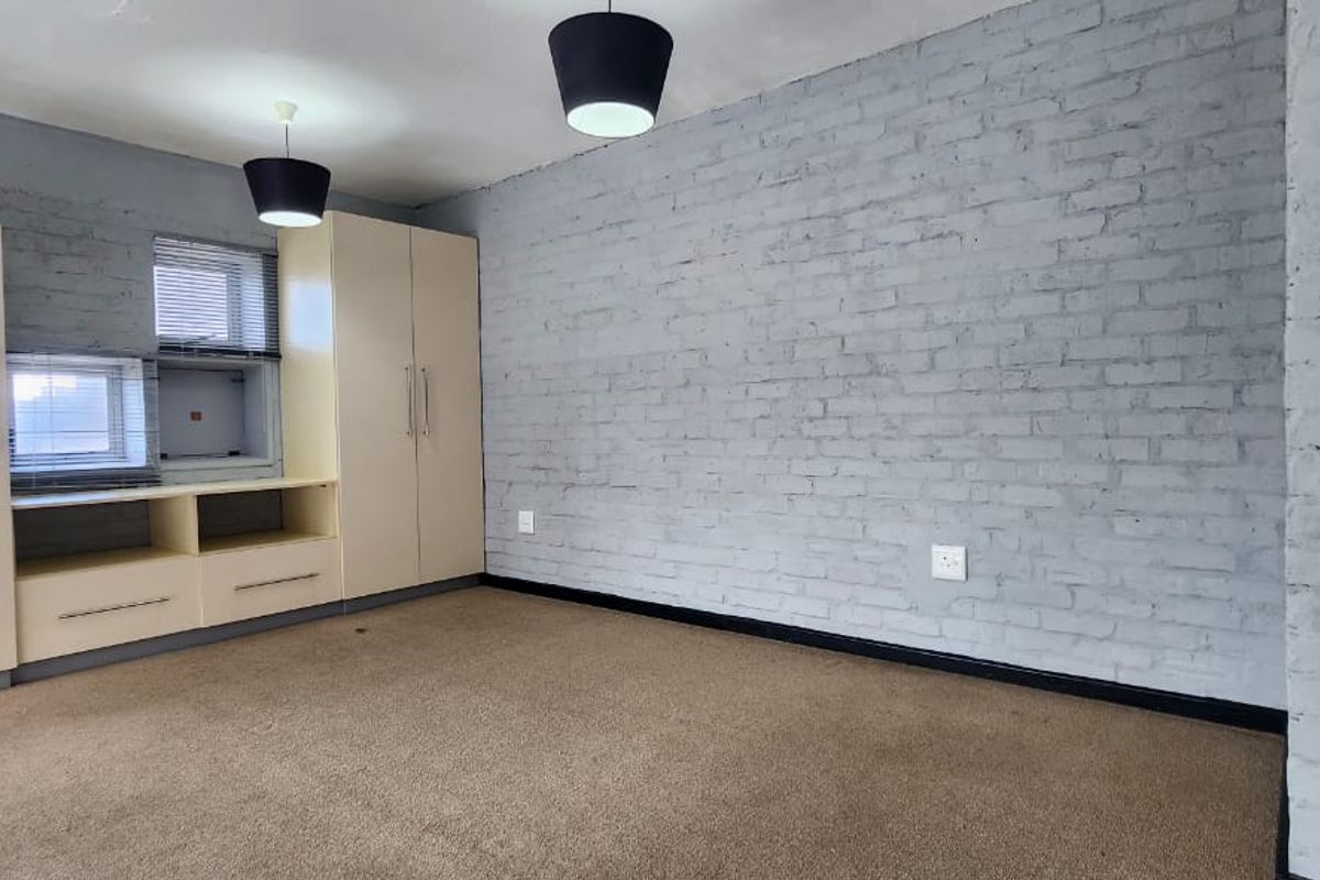 A spacious bedroom featuring exposed painted brick walls, built-in storage cupboards, and neutral carpeting, offering a blank canvas for personalization.