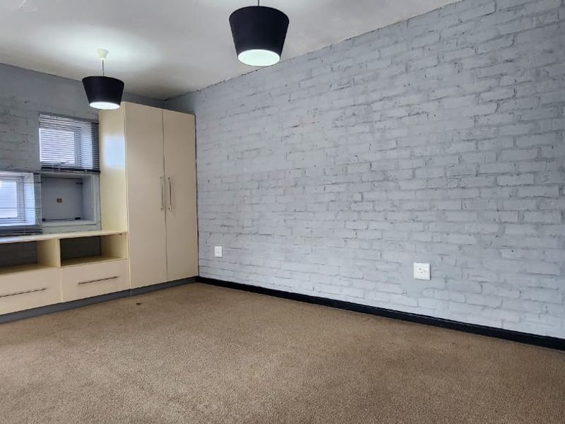 A spacious bedroom featuring exposed painted brick walls, built-in storage cupboards, and neutral carpeting, offering a blank canvas for personalization.