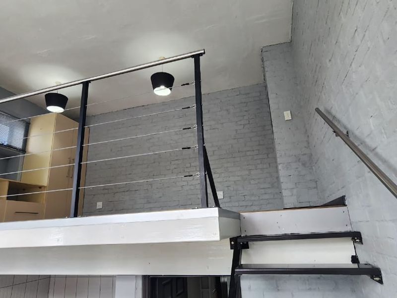 A mezzanine level featuring painted brick walls, a modern steel cable balustrade, and a staircase, offering an open-plan architectural feel.