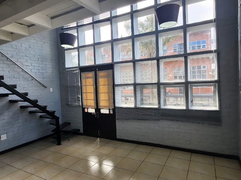 Spacious living area featuring double-volume ceilings, large grid windows, exposed brick walls, and a modern metal staircase.