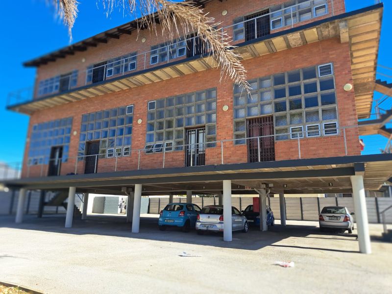 Exterior view of a multi-story apartment building featuring exposed brickwork, glass block windows, and a covered ground-level parking area.