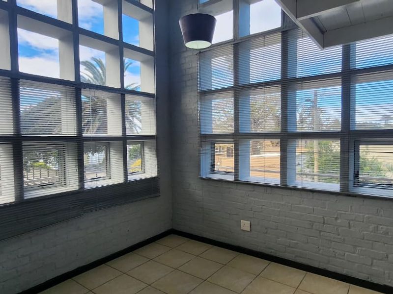 Bright open-plan living area featuring expansive grid windows, exposed brick walls, and neutral tiled flooring, offering a modern industrial aesthetic.