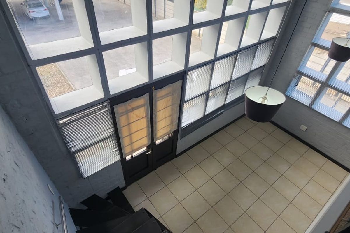 Spacious double-volume living area featuring large windows, tiled flooring, and a striking spiral staircase, offering a bright and airy atmosphere.