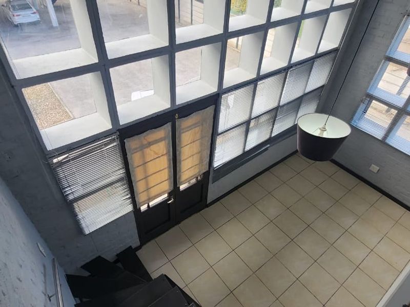 Spacious double-volume living area featuring large windows, tiled flooring, and a striking spiral staircase, offering a bright and airy atmosphere.