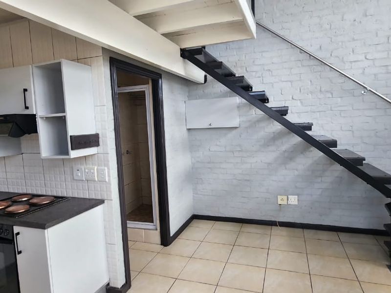 Open plan kitchen and living area featuring a metal staircase leading to a mezzanine level, exposed brick walls, and functional built-in cabinetry.