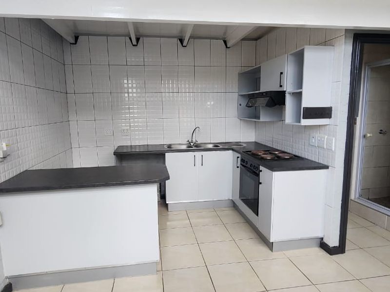 A functional kitchen featuring built-in cabinetry, laminate countertops, a stainless steel sink, and integrated oven and hob, with tiled flooring and backsplash.