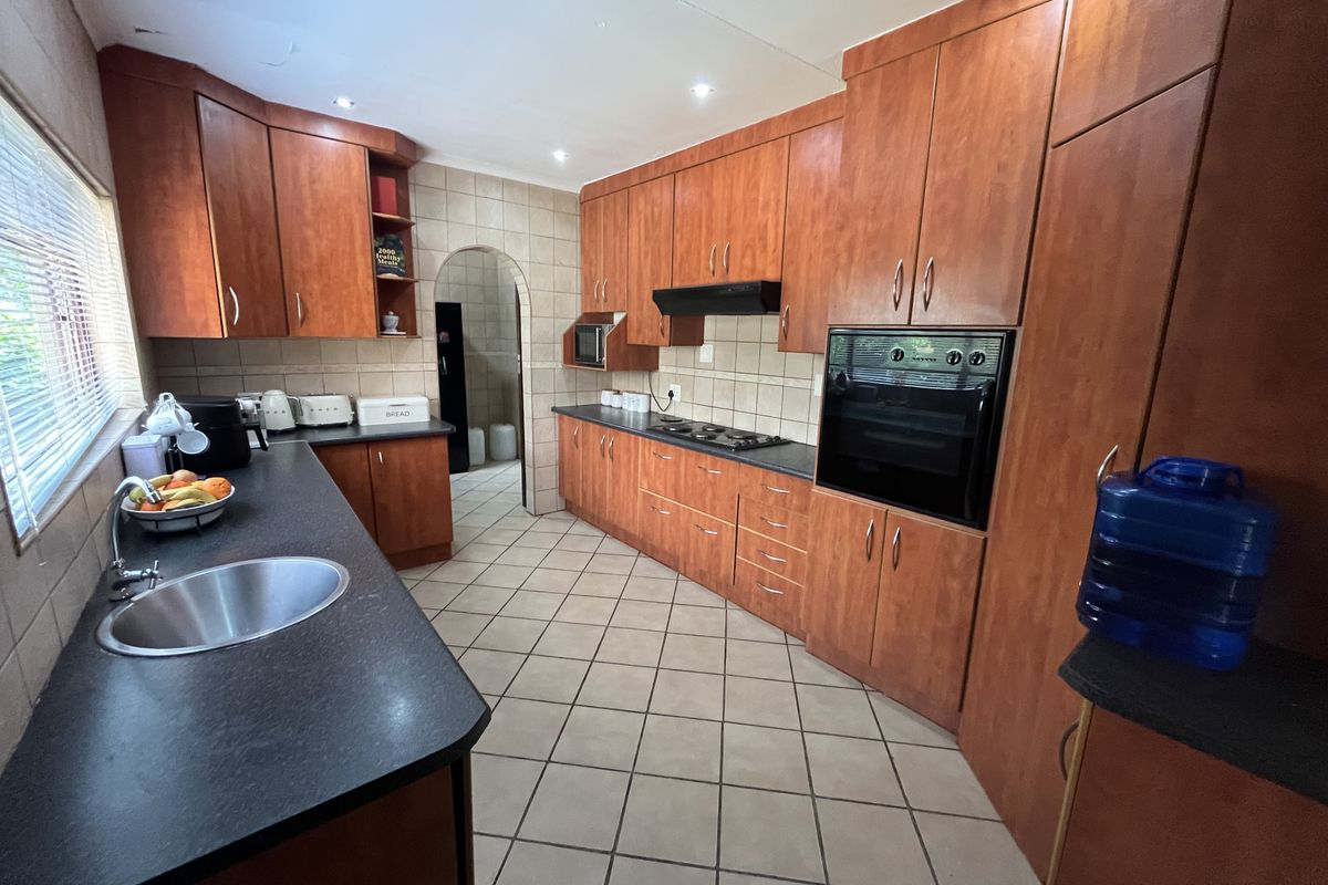 A functional kitchen featuring wood-finish cabinetry, dark countertops, built-in oven and hob, tiled flooring, and a distinctive arched doorway leading to an adjacent space.