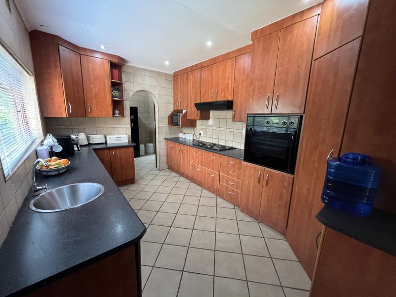 A functional kitchen featuring wood-finish cabinetry, dark countertops, built-in oven and hob, tiled flooring, and a distinctive arched doorway leading to an adjacent space.