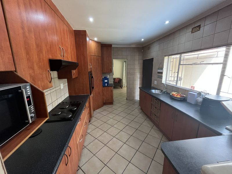 A functional kitchen featuring wood-tone cabinetry, dark laminate countertops, an electric hob with extractor, and tiled flooring throughout.