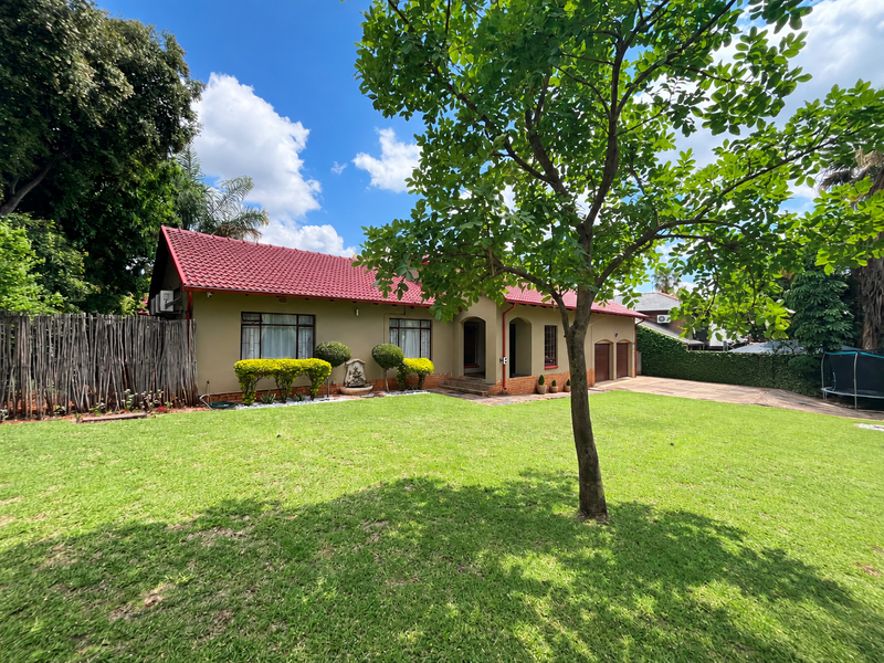 A well-maintained single-story house featuring a red tiled roof, a spacious front lawn, and a paved driveway leading to a double garage.