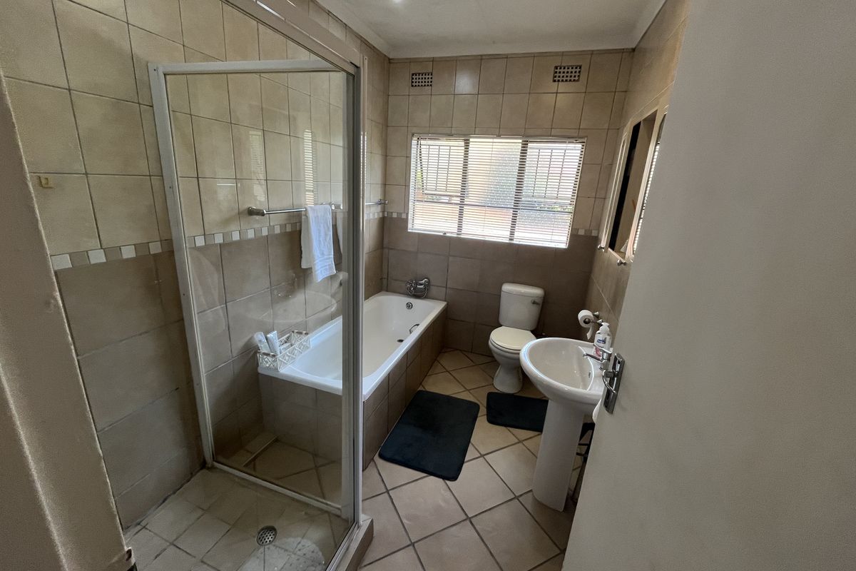 A functional bathroom featuring a separate shower enclosure, built-in bathtub, pedestal basin, and toilet with neutral wall and floor tiling.