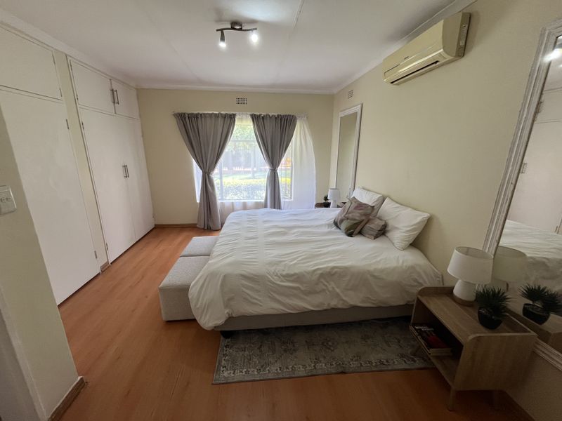 A well-lit bedroom featuring laminate flooring, ample built-in cupboard storage, and a wall-mounted split-system air conditioning unit.