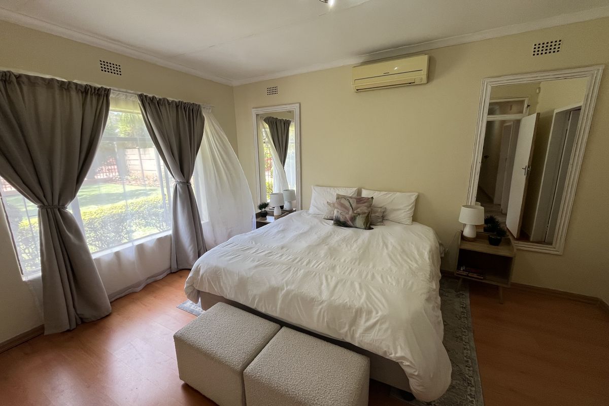 A well-lit bedroom featuring laminate flooring, an air conditioning unit, and large windows overlooking the garden.