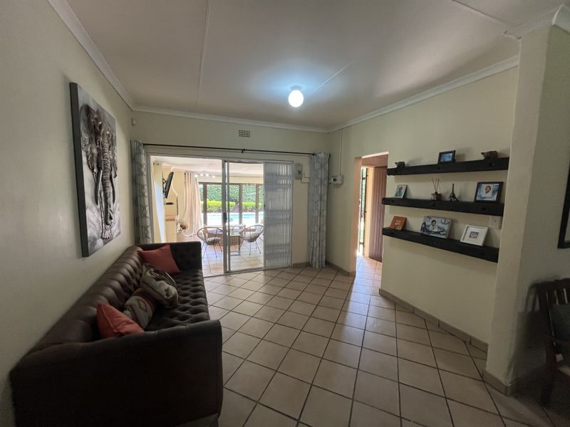 A living room featuring tiled flooring, built-in wall shelving, and a sliding glass door providing access to the outdoor patio and pool area.
