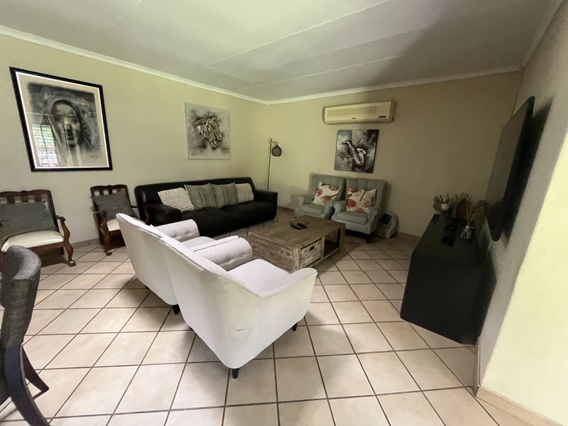 A spacious living room featuring ceramic tile flooring, a wall-mounted air conditioning unit, and coved ceilings, offering a comfortable and functional living space.