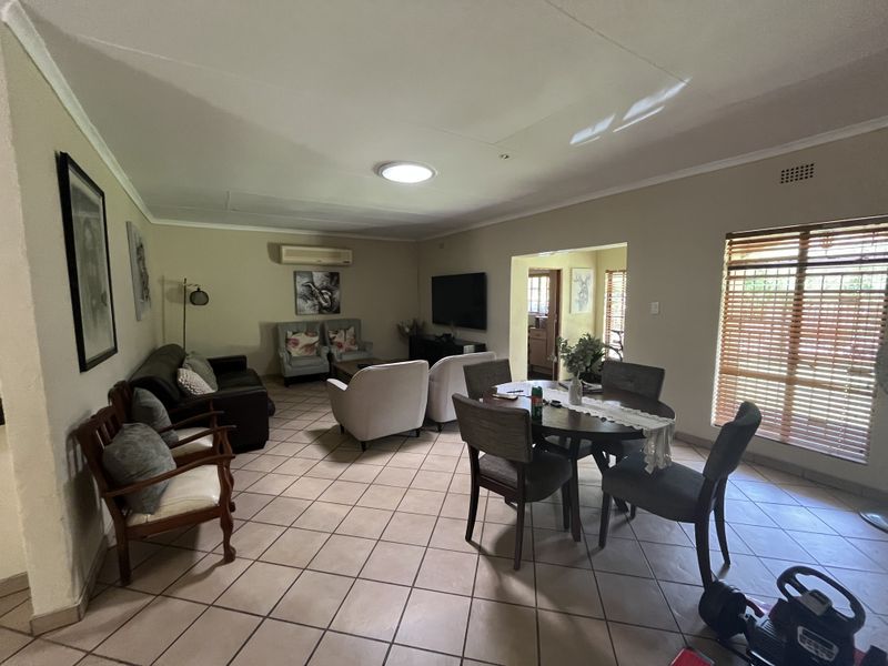 Spacious open-plan living and dining area featuring tiled flooring, air conditioning, and large windows with wooden blinds, offering a functional and versatile layout.