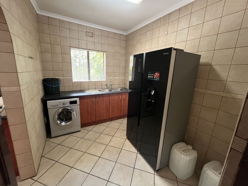 A functional laundry area featuring tiled walls and flooring, built-in cabinetry with a stainless steel sink, and dedicated space for laundry appliances.