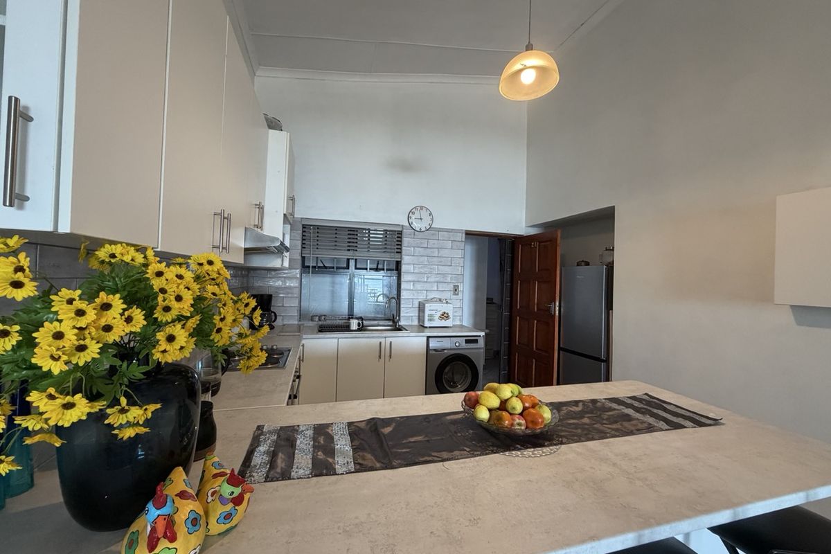 A functional kitchen featuring white cabinetry, subway tile backsplash, integrated laundry appliances, and a central breakfast counter with stone-look surfaces.