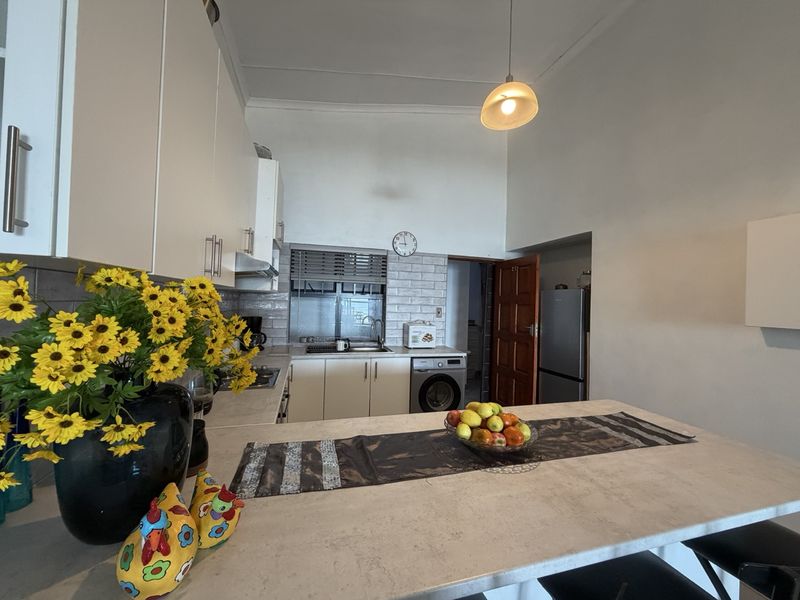 A functional kitchen featuring white cabinetry, subway tile backsplash, integrated laundry appliances, and a central breakfast counter with stone-look surfaces.