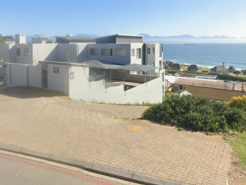 Exterior view of the apartment complex featuring a paved driveway, secure gated entrance, electric fencing, and covered parking bays with coastal views.