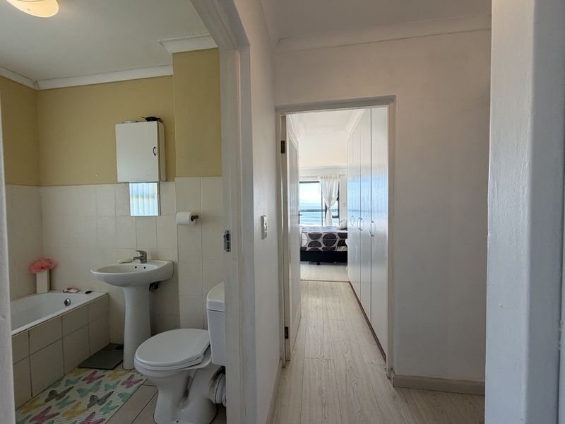 A functional bathroom featuring a pedestal basin, bathtub, and toilet, with an adjacent hallway leading to a bedroom with built-in storage.