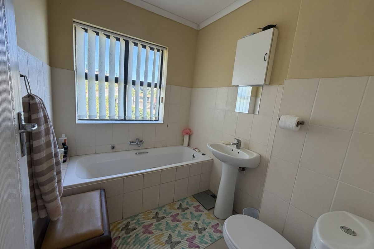 A functional bathroom featuring a bathtub, pedestal basin, toilet, and wall-mounted medicine cabinet with tiled splashbacks.