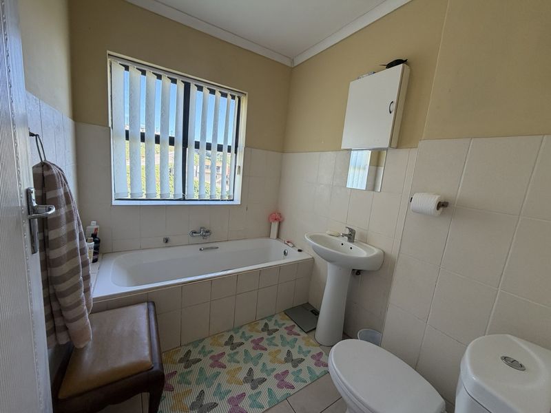 A functional bathroom featuring a bathtub, pedestal basin, toilet, and wall-mounted medicine cabinet with tiled splashbacks.