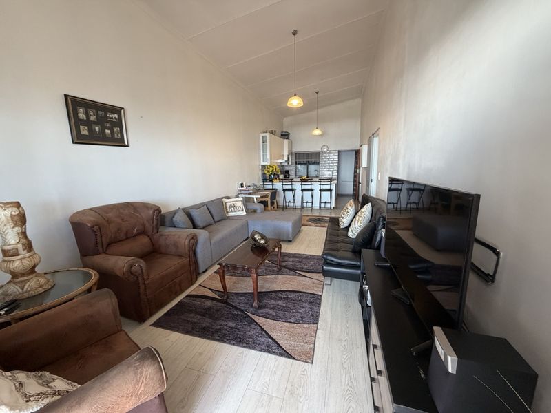 An open-plan living and kitchen area featuring laminate flooring, modern pendant lighting, and a functional kitchen with a breakfast island and subway tile backsplash.