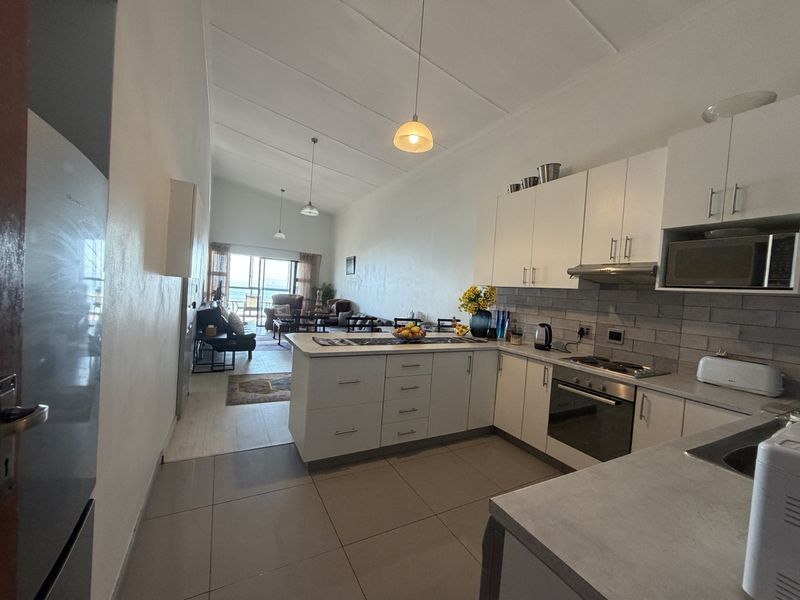 Open-plan kitchen and living area featuring modern white cabinetry, built-in appliances, tiled flooring, and direct access to a balcony with ocean views.