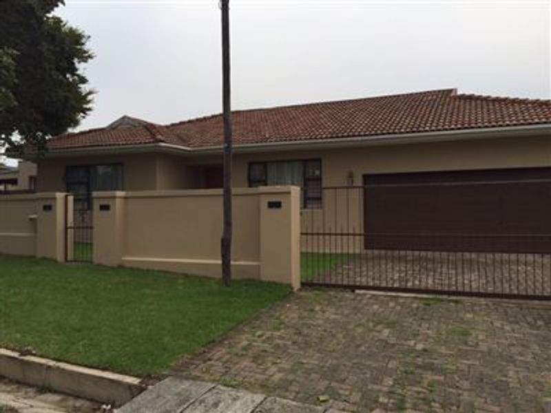 Front elevation of a single-story house featuring a tiled roof, paved driveway, secure metal gate, and a private boundary wall with a lawn.
