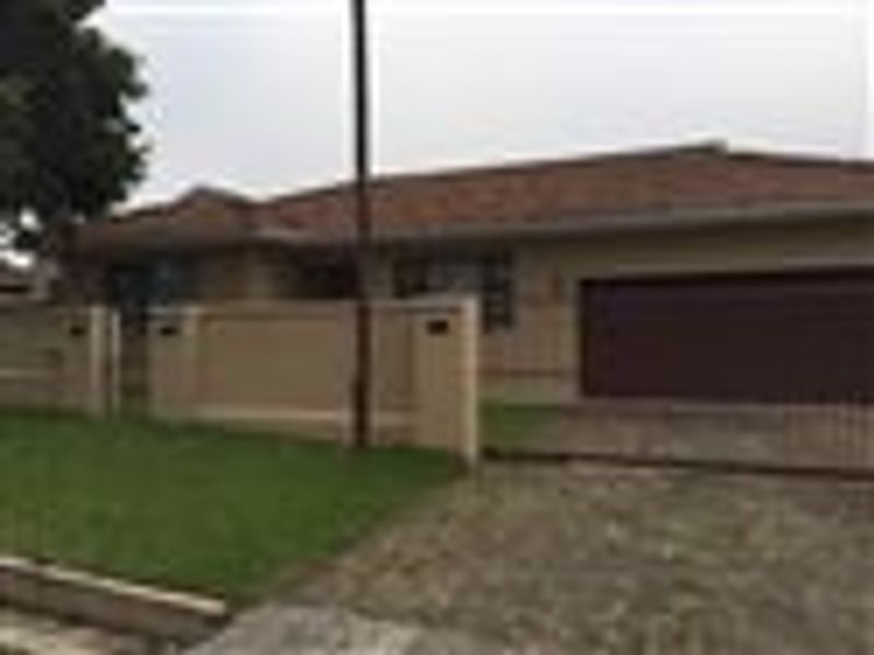Front view of a single-story house featuring a tiled roof, a paved driveway, a garage, and a front boundary wall with a lawn.