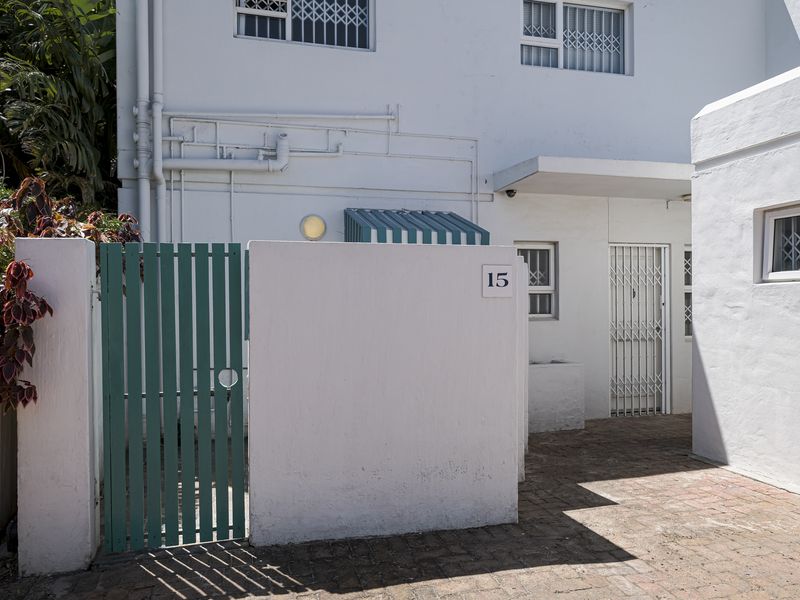Front entrance of the townhouse featuring a paved courtyard, security gate, and white rendered walls with visible exterior plumbing.