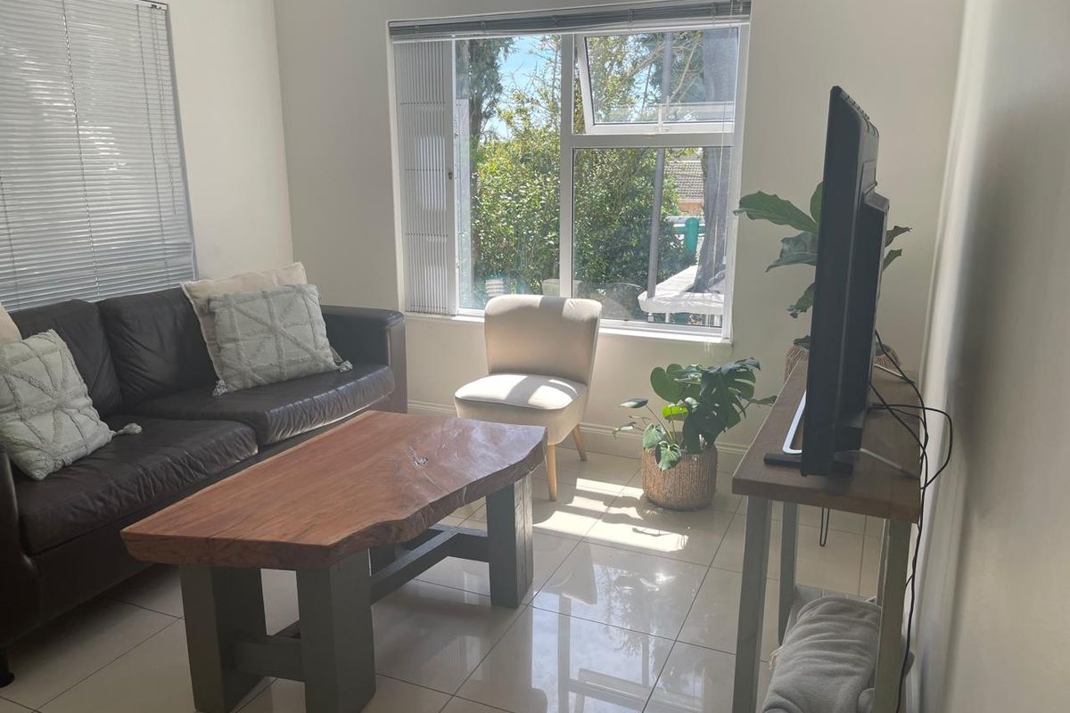 A bright living room featuring tiled flooring and large windows with venetian blinds, offering a view of the garden.