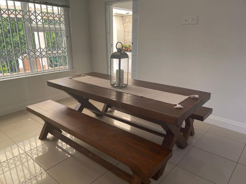 A bright dining room featuring neutral tiled flooring, clean white walls, and a secure window with a fitted security gate.