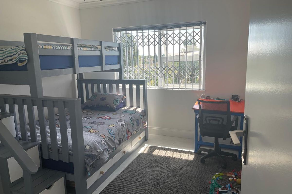 A well-lit bedroom featuring a window with a security gate, neutral walls, and standard ceiling finishes.