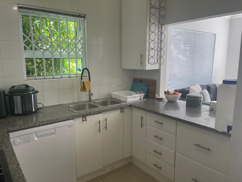 Functional kitchen featuring granite countertops, white cabinetry, double basin sink, and tiled backsplash, with a convenient pass-through window to the living area.