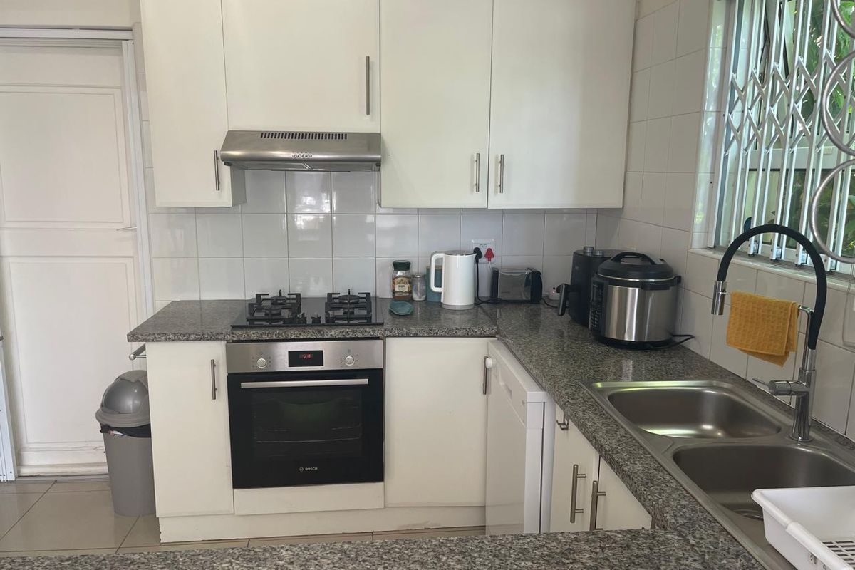 A functional kitchen featuring white cabinetry, granite countertops, a built-in oven with gas hob, and a double bowl sink with a modern faucet.