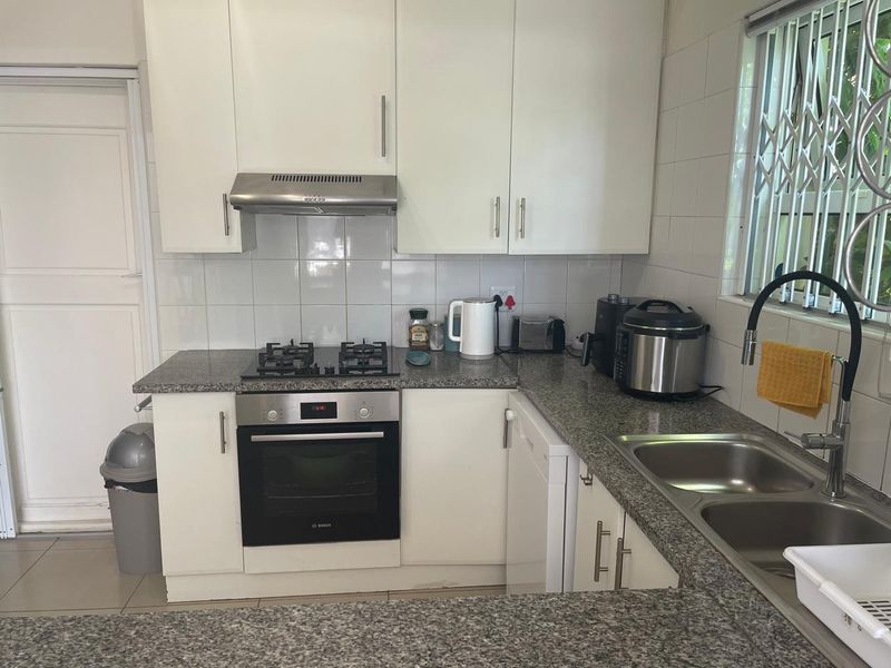 A functional kitchen featuring white cabinetry, granite countertops, a built-in oven with gas hob, and a double bowl sink with a modern faucet.
