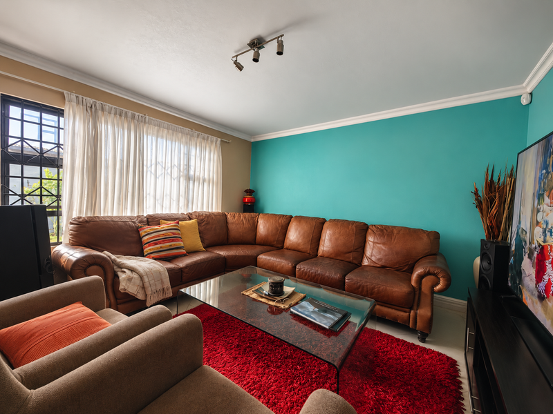 A comfortable living room featuring a vibrant teal accent wall, ceiling coving, and track lighting, with large windows fitted with security bars.